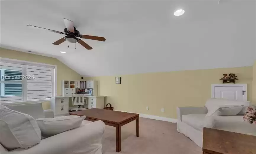 Carpeted living room featuring ceiling fan and vaulted ceiling