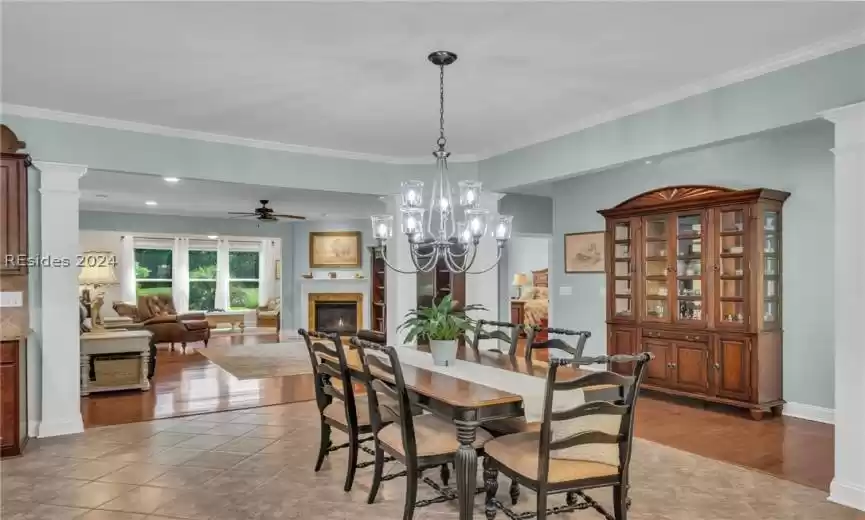 Dining area featuring ornate columns, crown molding, light tile floors, and ceiling fan with notable chandelier