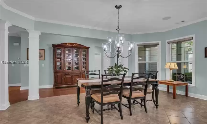 Tiled dining space featuring ornamental molding, decorative columns, and a chandelier