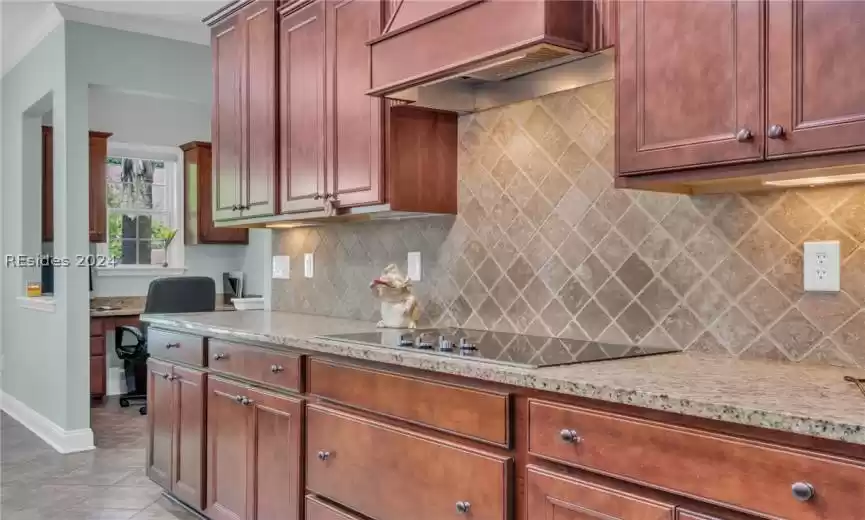 Kitchen with light stone counters, light tile floors, tasteful backsplash, crown molding, and black electric stovetop