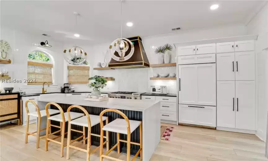 Kitchen featuring double oven range, custom range hood, tasteful backsplash, dark stone countertops, and white cabinets