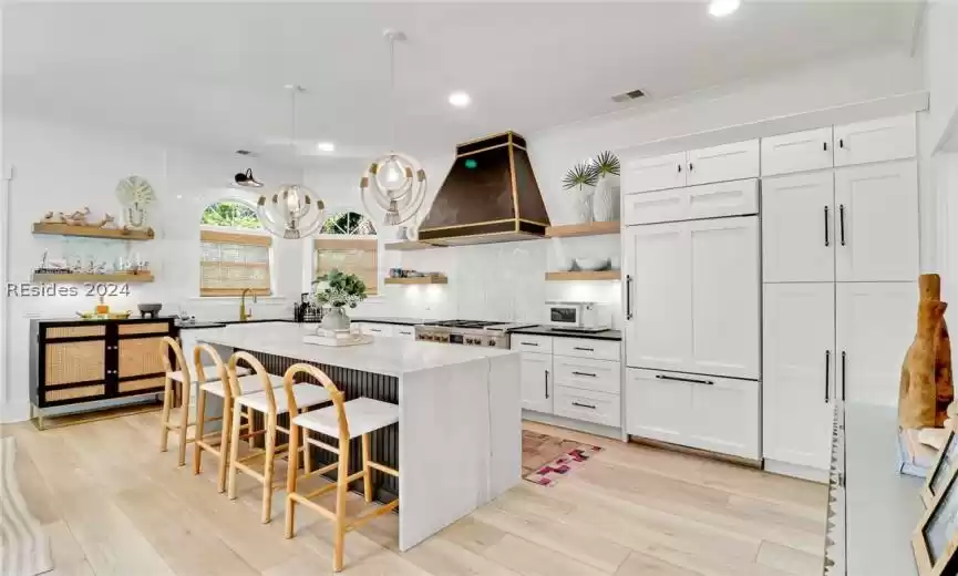 Kitchen with white cabinets, backsplash, a kitchen island, and custom exhaust hood