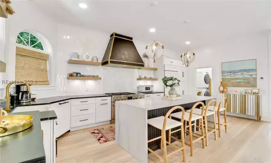 Kitchen with white cabinetry, backsplash, custom range hood, a kitchen island, and light hardwood / wood-style floors