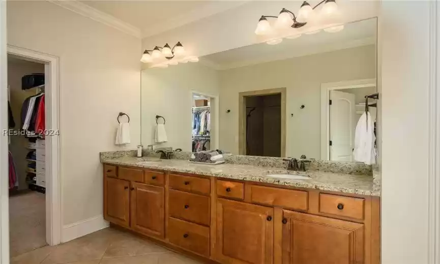 Primary bathroom with diagonal tile flooring also has a long vanity with two sinks and lots of storage below as well as a linen closet.