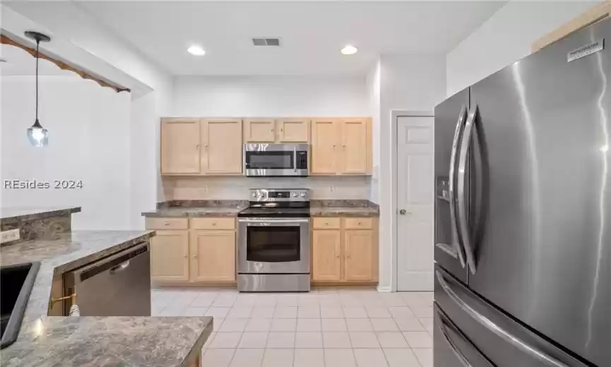 Kitchen with decorative light fixtures, appliances with stainless steel finishes, light tile floors, and light brown cabinets