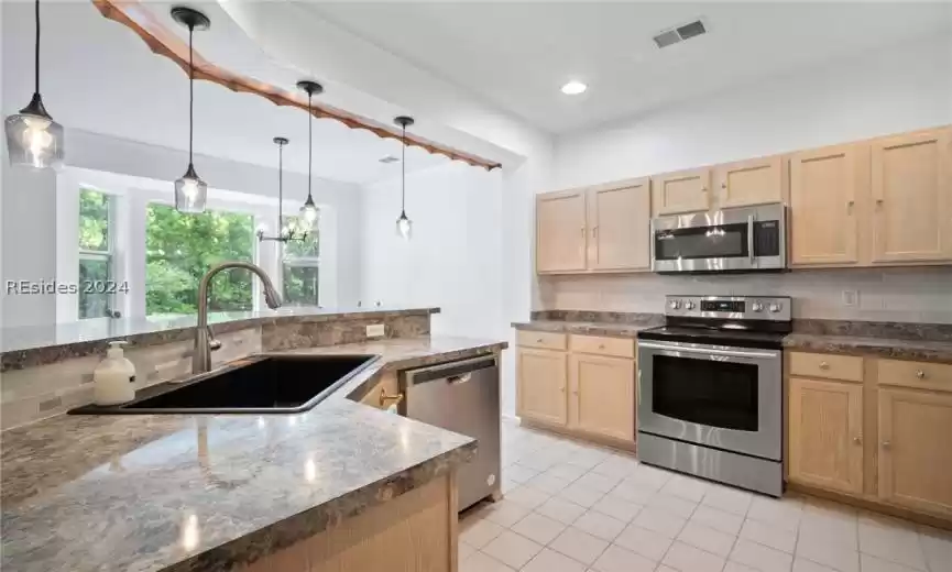 Kitchen with appliances with stainless steel finishes, hanging light fixtures, light tile flooring, tasteful backsplash, and sink