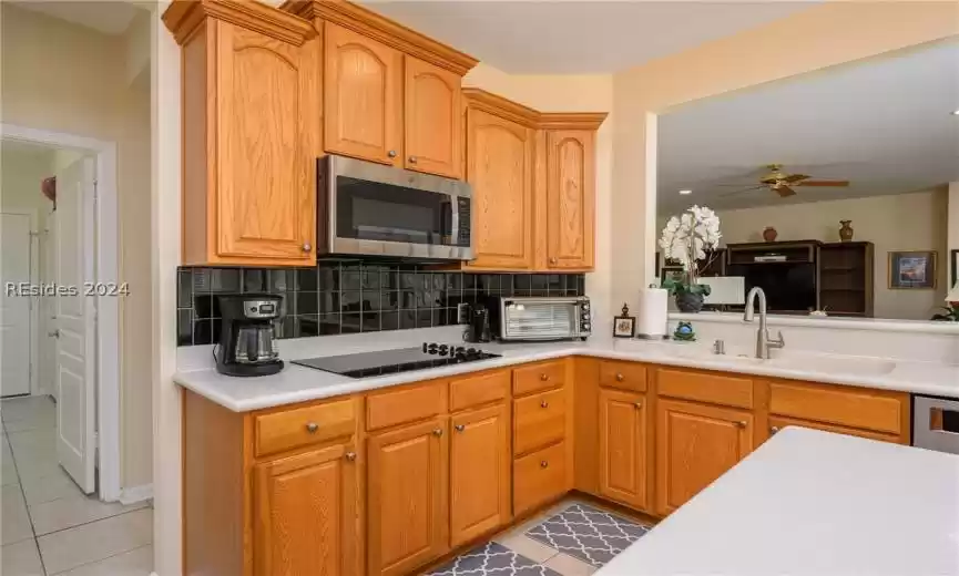 Kitchen with tasteful backsplash, light tile floors, black electric cooktop, ceiling fan, and sink