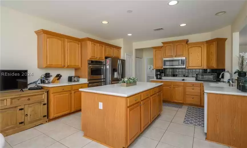 Kitchen with a kitchen island, tasteful backsplash, sink, appliances with stainless steel finishes, and light tile floors