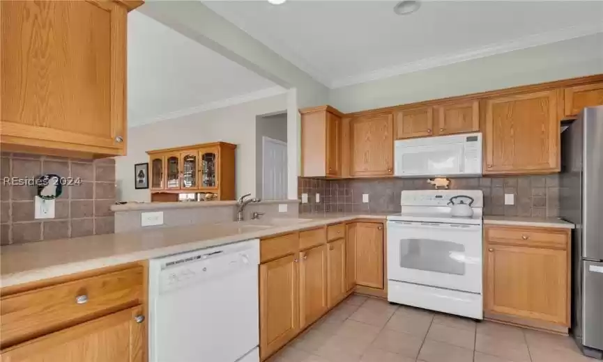 Kitchen with backsplash, sink, light tile flooring, white appliances, and ornamental molding