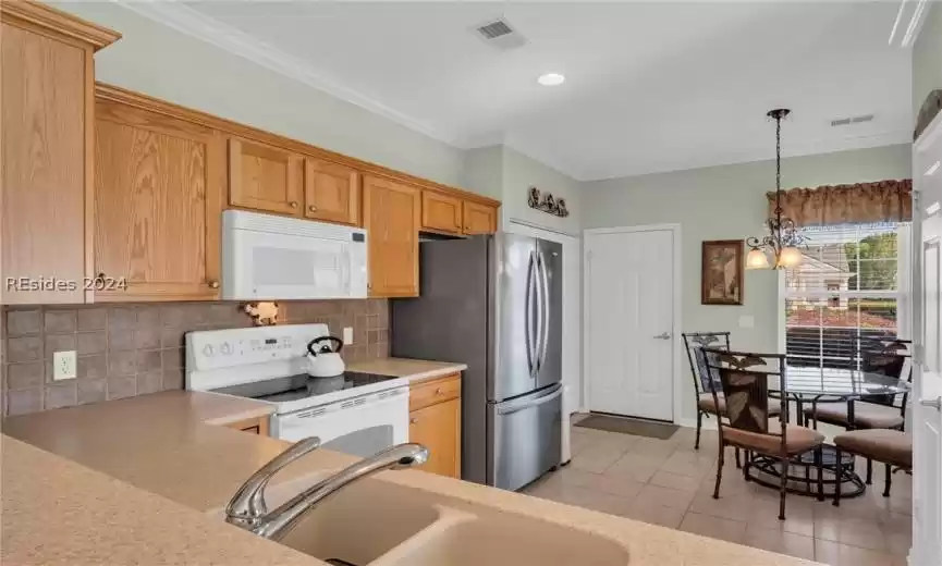Kitchen with an inviting chandelier, backsplash, sink, white appliances, and decorative light fixtures
