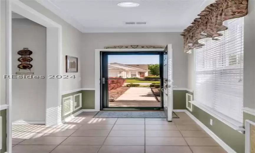Entryway featuring ornamental molding, light tile floors.