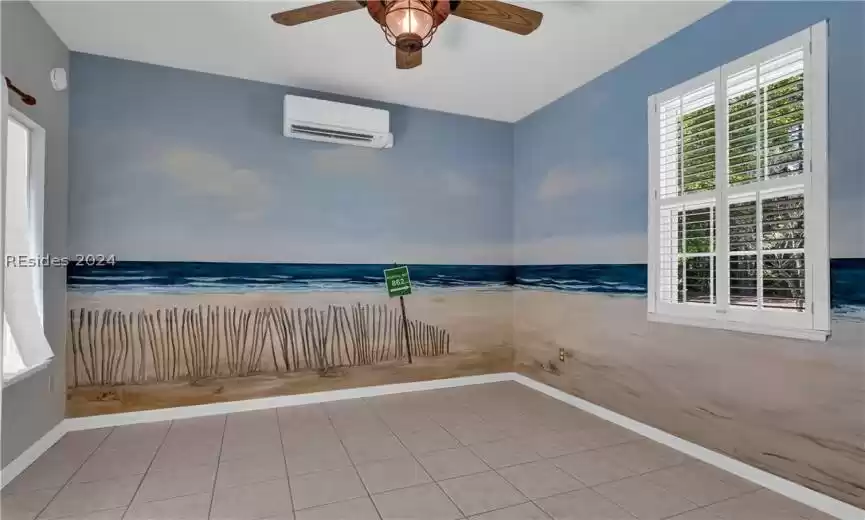 Empty room with ceiling fan, light tile floors, and an AC wall unit