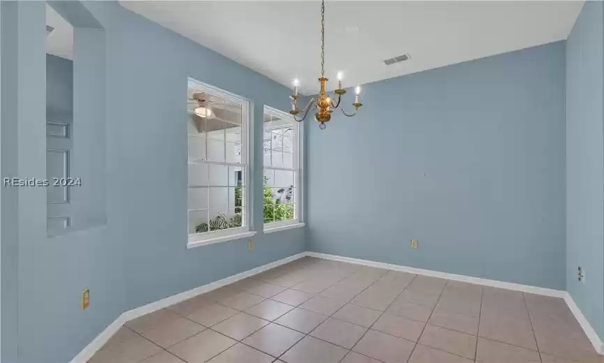 Empty room featuring ceiling fan with notable chandelier and light tile floors