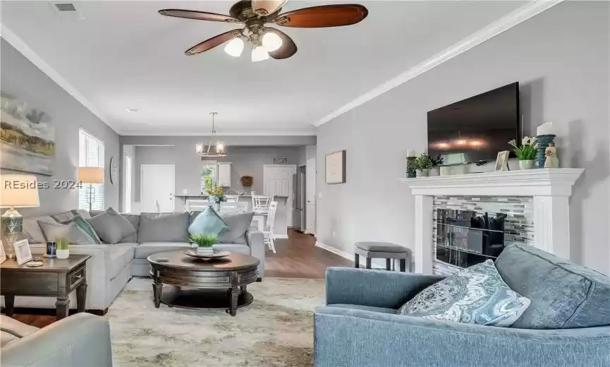 Living room featuring ornamental molding, ceiling fan with notable chandelier, light wood-type flooring, and a fireplace