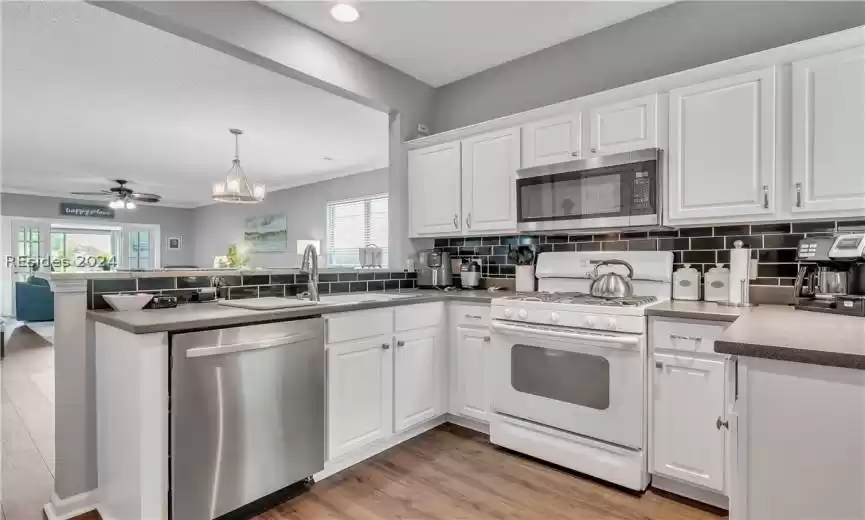 Kitchen with white cabinets, ceiling fan with notable chandelier, light hardwood / wood-style flooring, backsplash, and stainless steel appliances