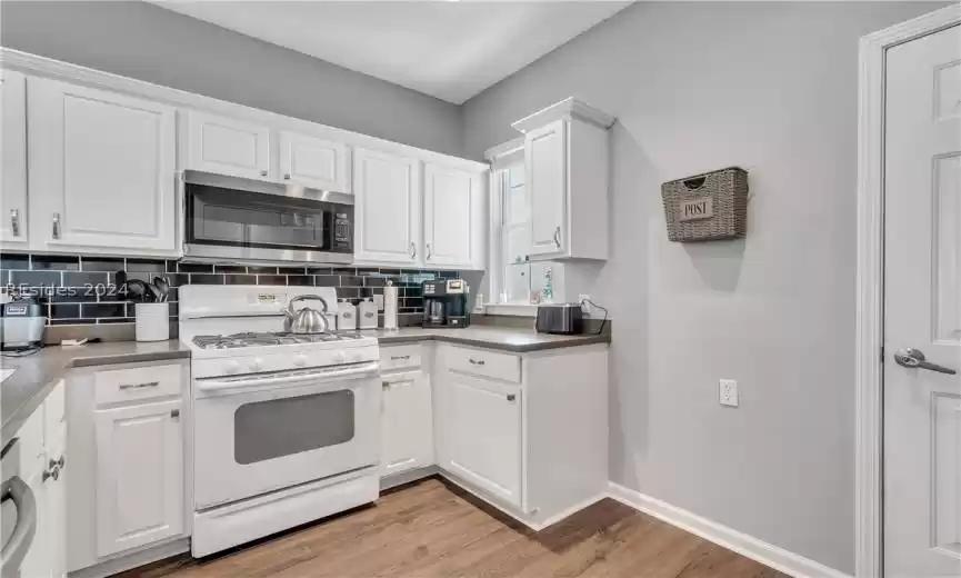 Kitchen with white cabinetry, tasteful backsplash, light hardwood / wood-style floors, and white range with gas cooktop