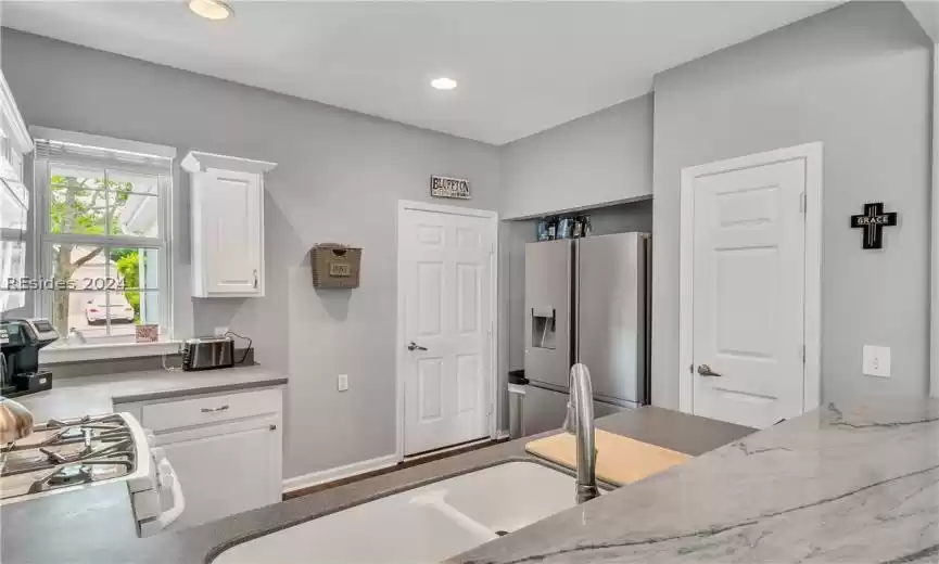 Kitchen with white gas range oven, stainless steel fridge, light stone countertops, and white cabinetry