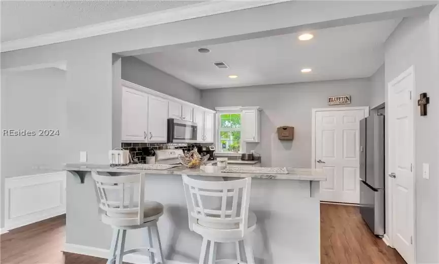 Kitchen with white cabinets, wood-type flooring, a kitchen breakfast bar, and stainless steel appliances