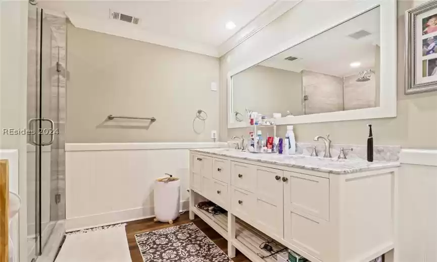 Primary Bathroom with a shower with door, hardwood / wood-style floors, dual bowl vanity, and crown molding