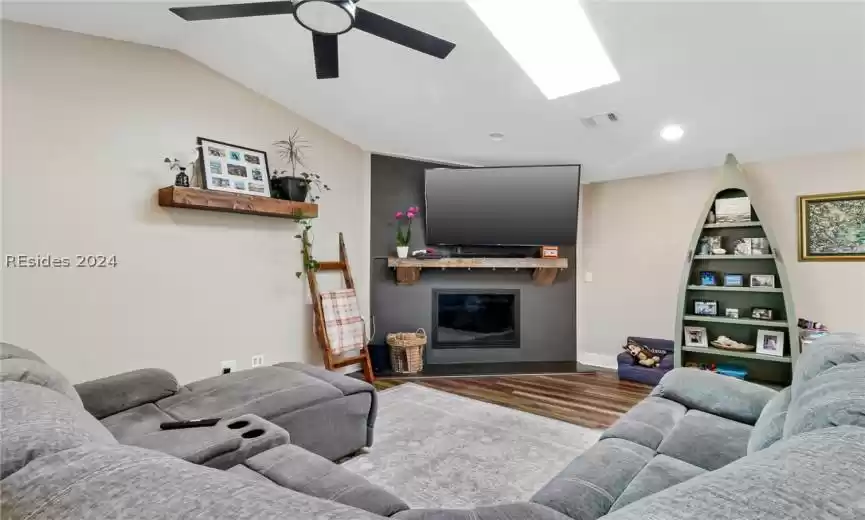 Living room with a skylight,  hardwood/LVP / wood-style flooring, and ceiling fan