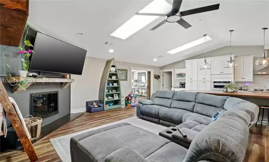 Living room featuring hardwood / wood-style flooring, lofted ceiling with skylight, and ceiling fan