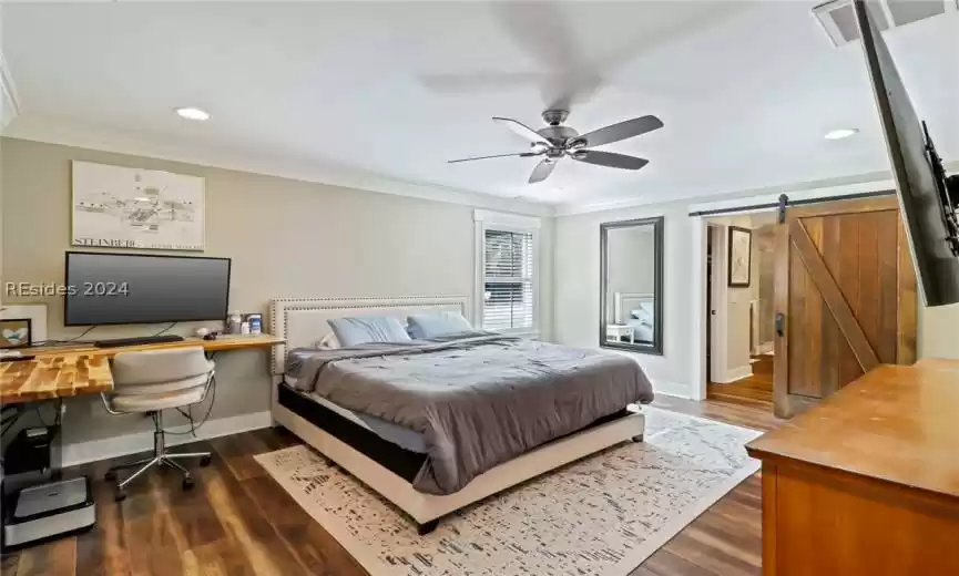 Primary Bedroom with ceiling fan, dark hardwood / wood-style flooring, crown molding, and a barn door