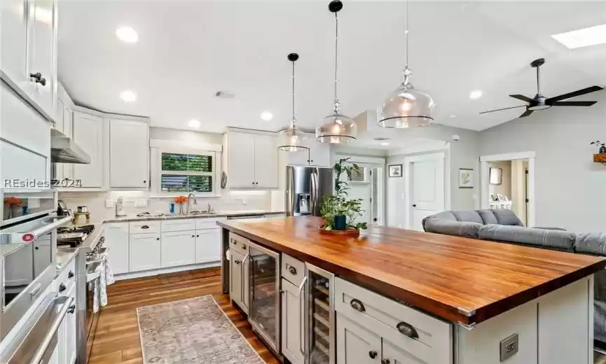 Kitchen featuring decorative light fixtures, a kitchen island, backsplash, butcher block counters, and white cabinetry