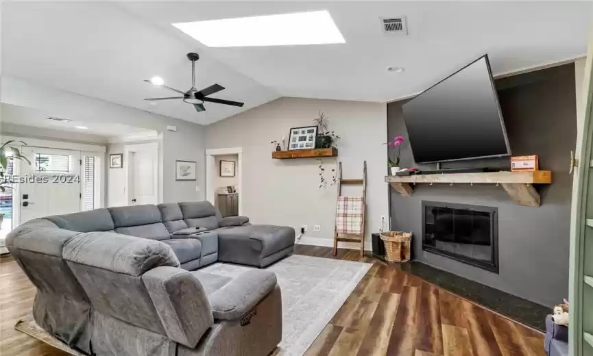 Living room with ceiling fan, hardwood /LVP wood-style floors, and vaulted ceiling with skylight