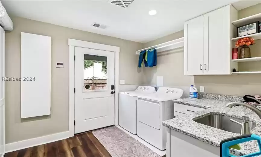 Laundry area with dark wood-type flooring, washing machine and dryer, cabinets, and sink