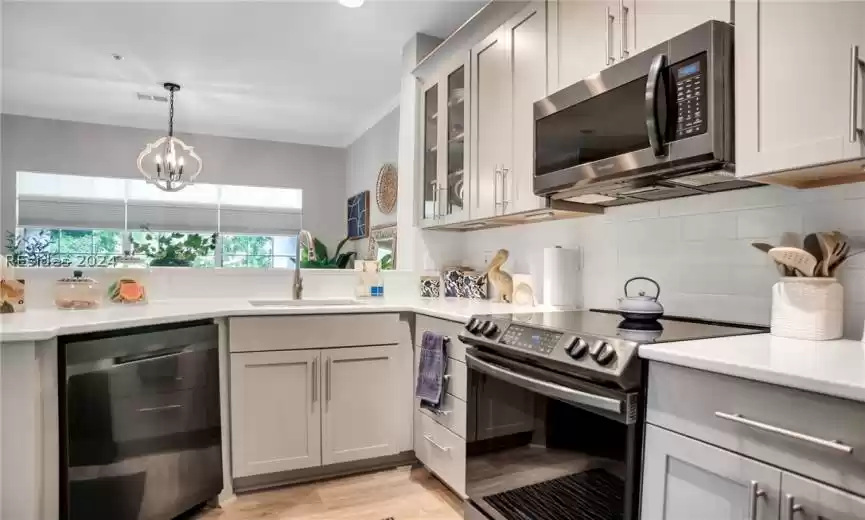 Kitchen with electric stove, light hardwood / wood-style floors, backsplash, dishwashing machine, and an inviting chandelier