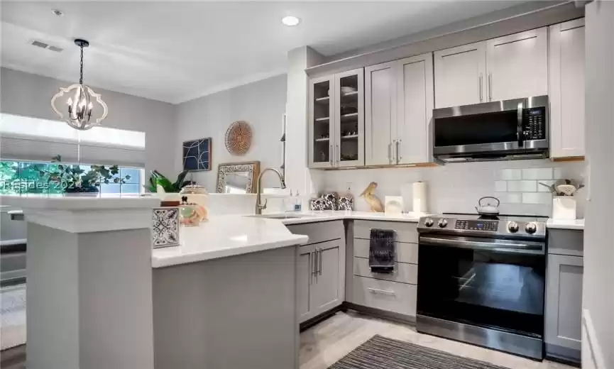 Kitchen with backsplash, kitchen peninsula, electric stove, and gray cabinets