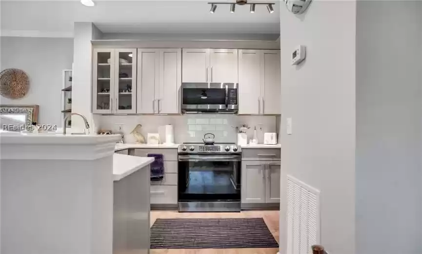Kitchen with appliances with stainless steel finishes, tasteful backsplash, light hardwood / wood-style flooring, kitchen peninsula, and track lighting