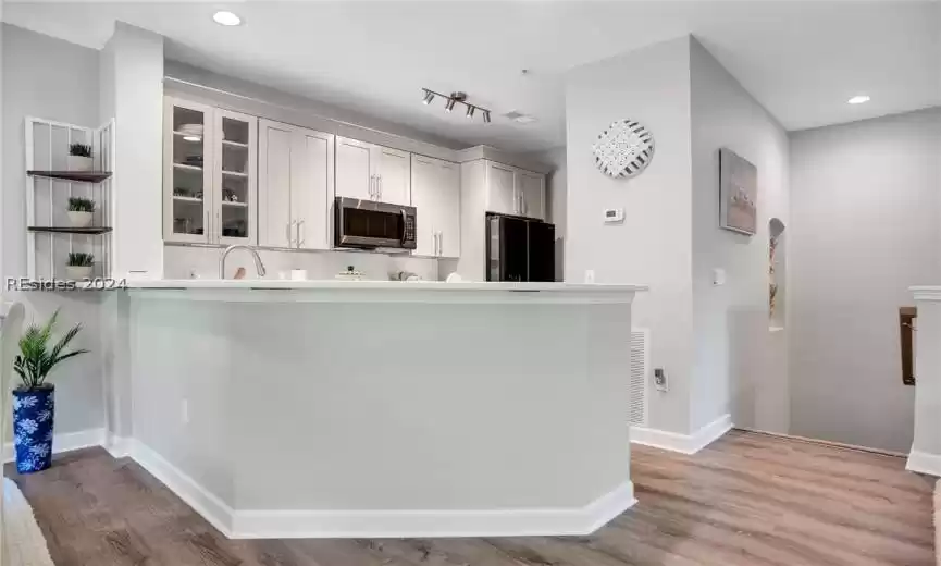 Kitchen featuring black fridge, light hardwood / wood-style flooring, rail lighting, kitchen peninsula, and sink