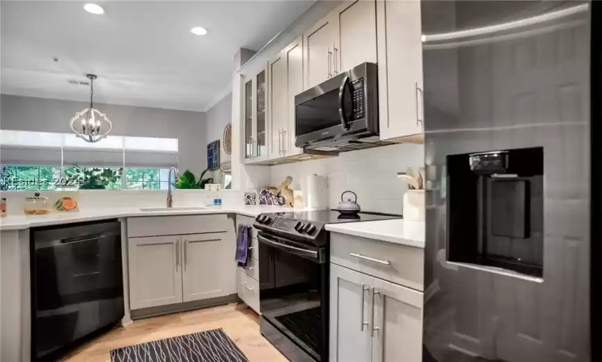 Kitchen featuring backsplash, light hardwood / wood-style floors, black appliances, sink, and a chandelier