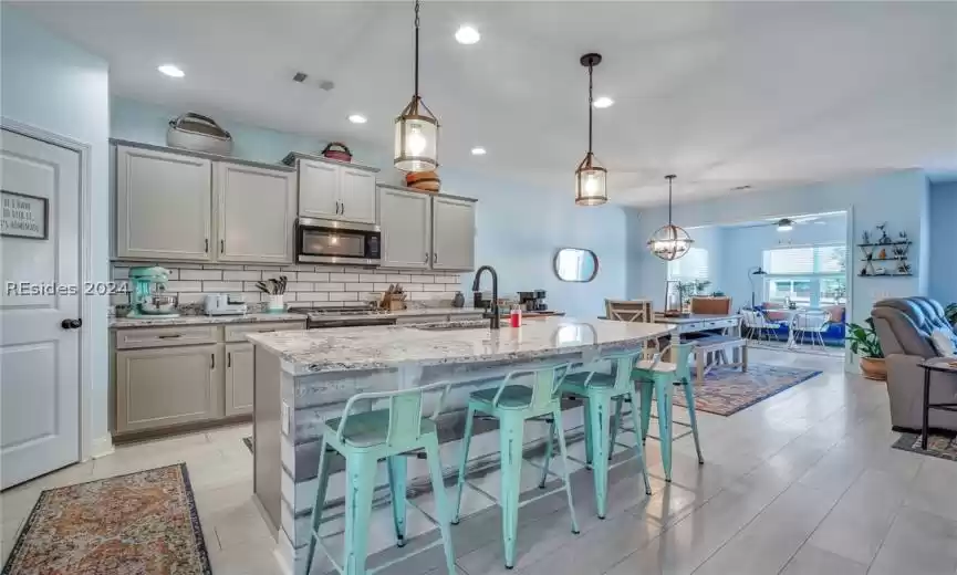 Kitchen with pendant lighting, a kitchen island with sink, backsplash, sink, and a kitchen bar