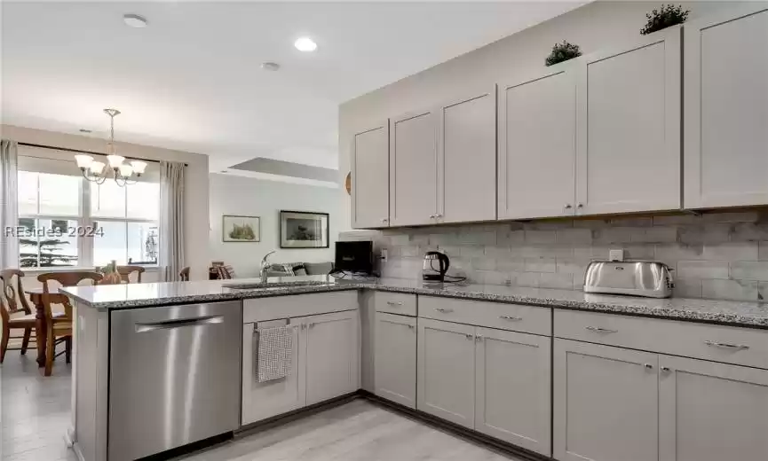 Kitchen with light wood-type flooring, tasteful backsplash, kitchen peninsula, and dishwasher