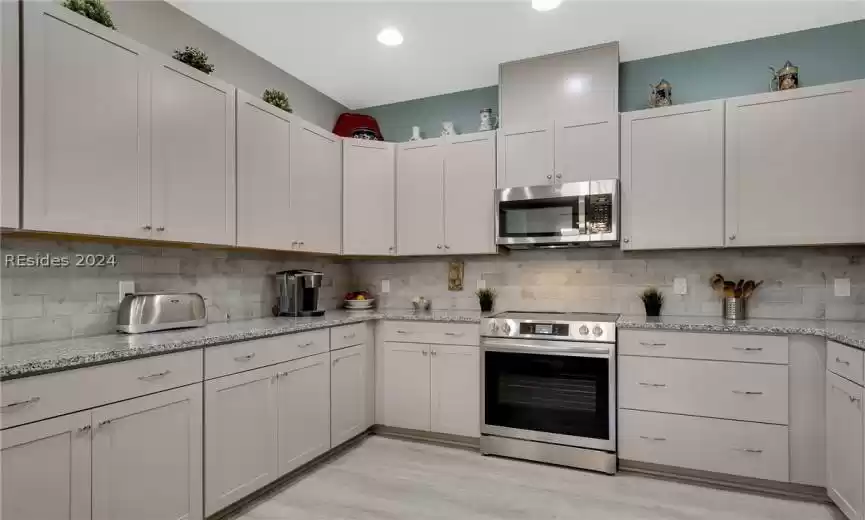 Kitchen featuring tasteful backsplash, appliances with stainless steel finishes, light hardwood / wood-style floors, and white cabinetry