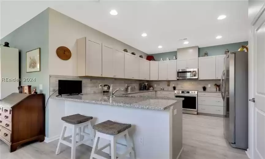 Kitchen with kitchen peninsula, backsplash, stainless steel appliances, light hardwood / wood-style floors, and light stone counters