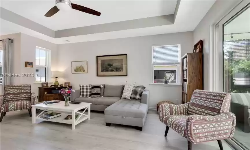 Living room featuring light hardwood / wood-style floors, ceiling fan, and a tray ceiling