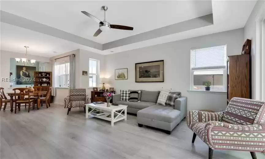 Living room featuring ceiling fan with notable chandelier, a raised ceiling, and light hardwood / wood-style floors