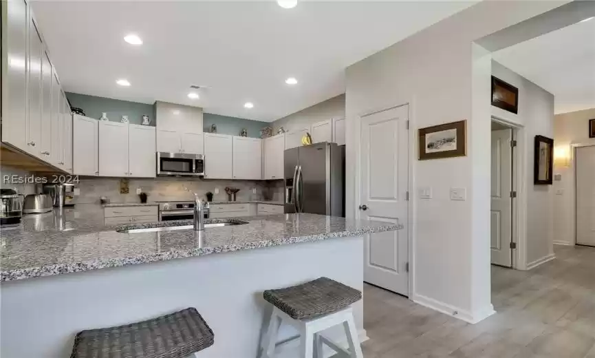 Kitchen featuring light hardwood / wood-style floors, appliances with stainless steel finishes, tasteful backsplash, and light stone counters