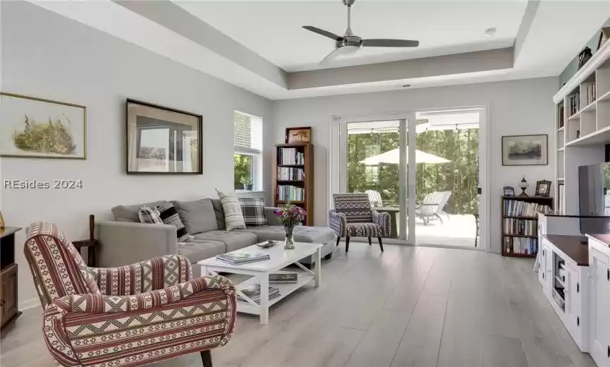 Living room with light hardwood / wood-style flooring, ceiling fan, and a tray ceiling