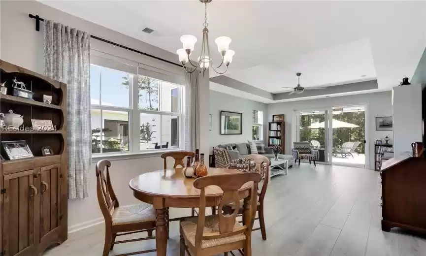 Dining room with ceiling fan with notable chandelier, light hardwood / wood-style flooring, and a tray ceiling