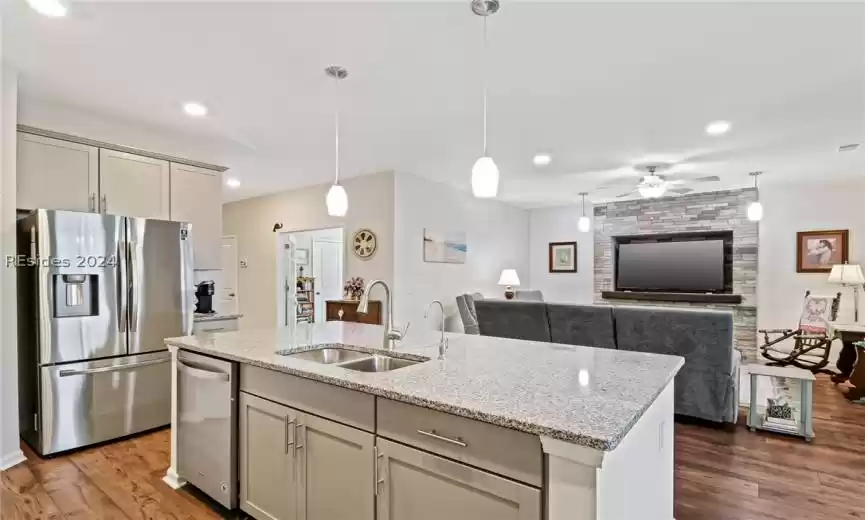 Kitchen featuring light stone counters, sink, hardwood / wood-style floors, stainless steel appliances, and a kitchen island with sink