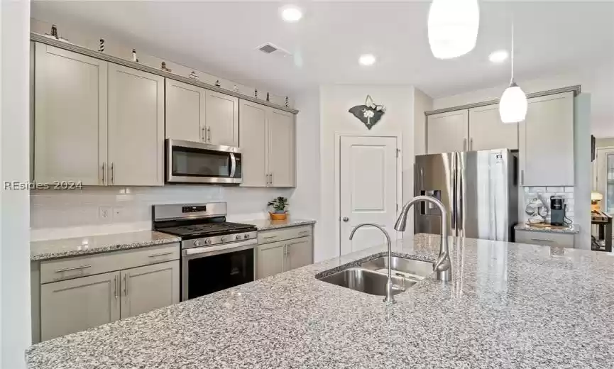 Kitchen featuring decorative light fixtures, stainless steel appliances, sink, light stone counters, and tasteful backsplash