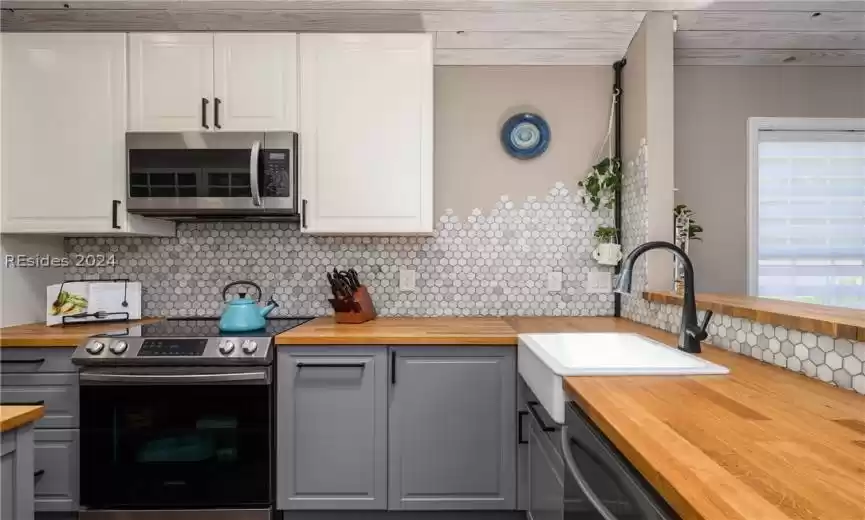 Kitchen featuring white cabinets, butcher block countertops, backsplash, and stainless steel appliances