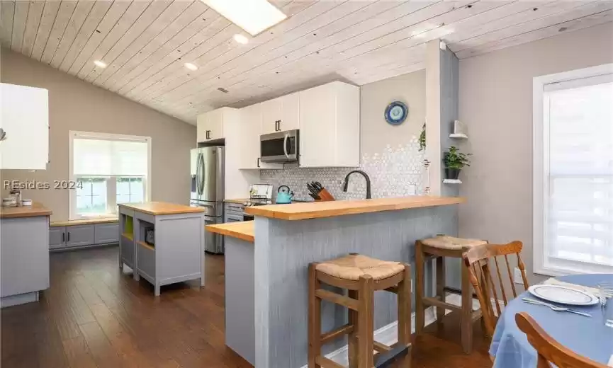 Kitchen with dark wood-type flooring, backsplash, stainless steel appliances, a kitchen bar, and butcher block counters